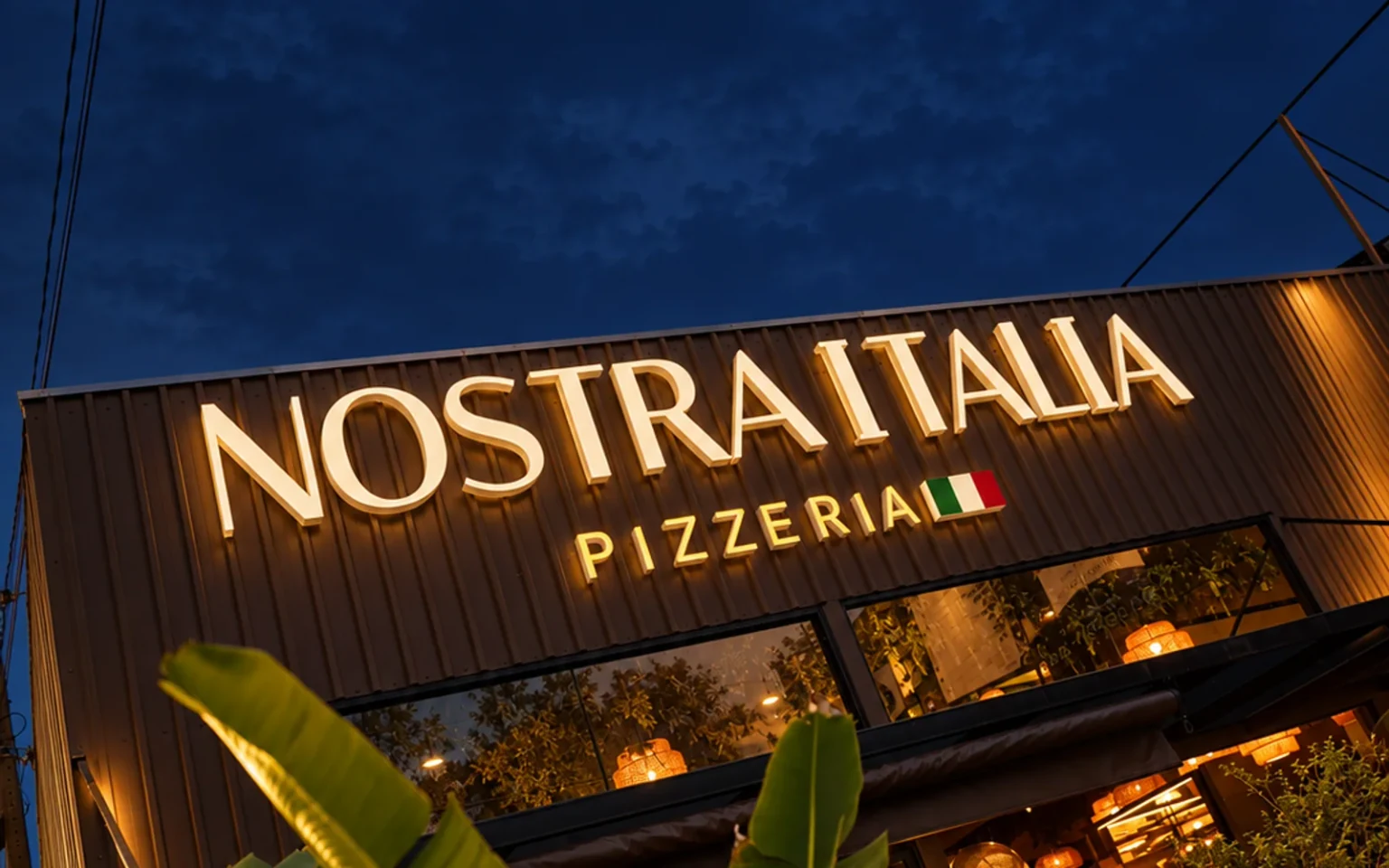 Fachada real da Nostra Itália iluminada à noite, com a identificação do estabelecimento