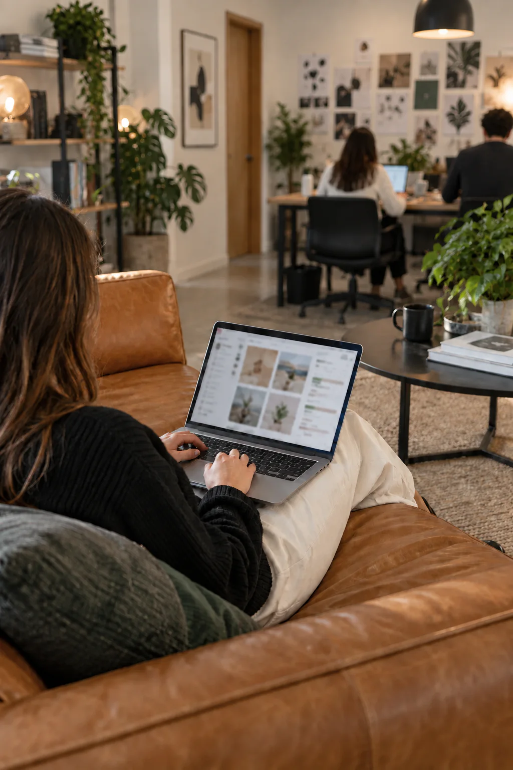 Profissional vista de costas planejando conteúdo para redes sociais em um notebook, sentada em um sofá de couro caramelo