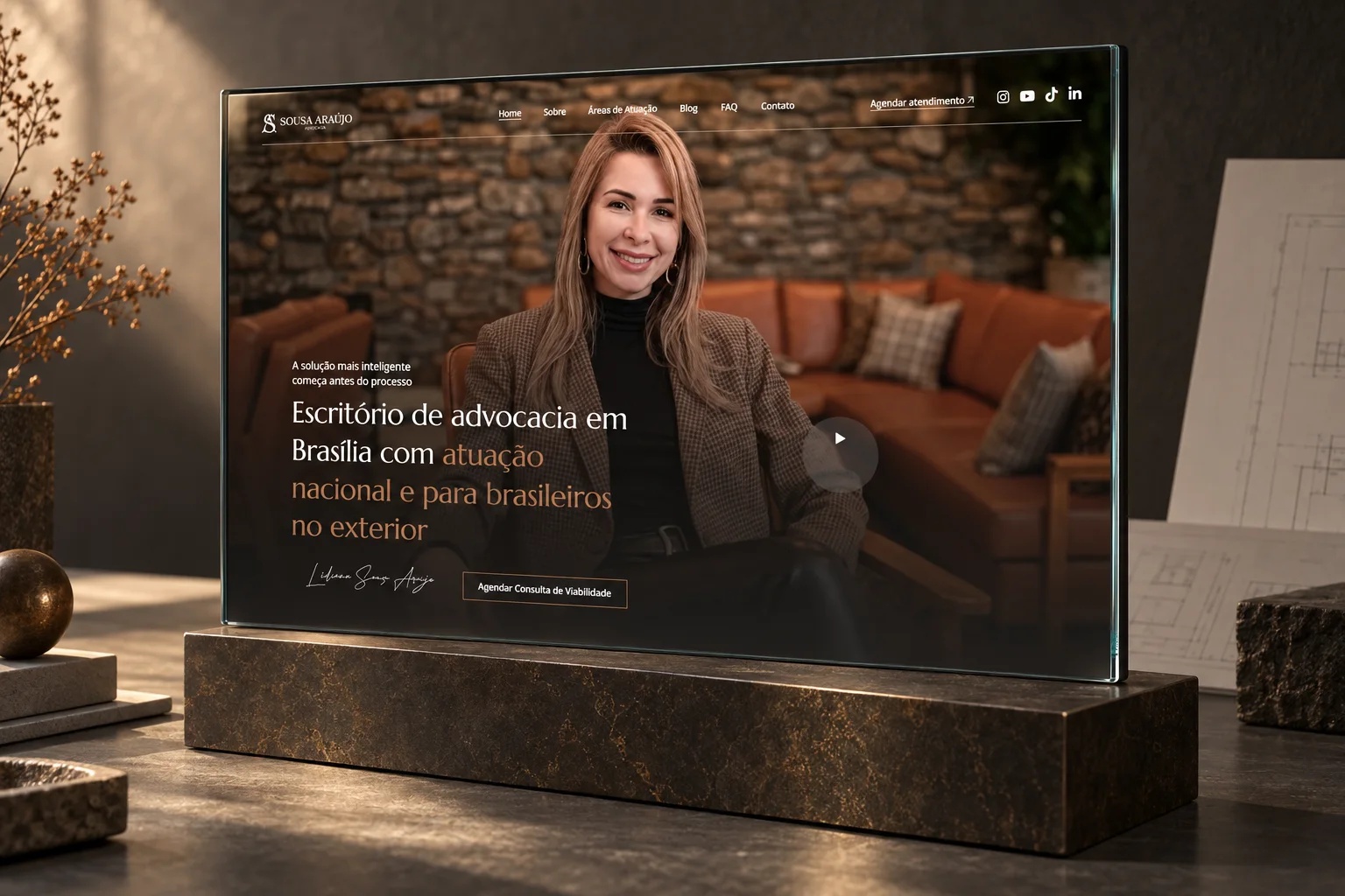 Montagem editorial com a página inicial real do site Sousa Araújo Advocacia em uma tela de vidro